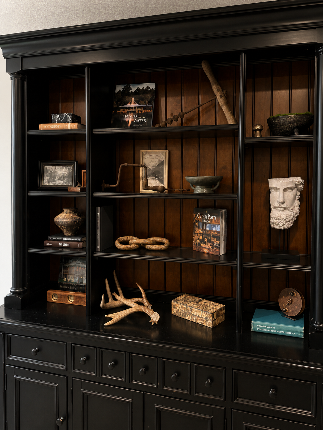 Landmark Construction — black hutch cabinet with antlers, books, and sculpture