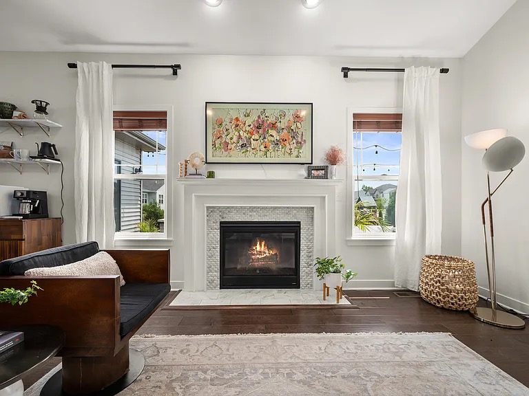 Bright living room with a white fireplace mantel, floral art, and soft linen curtains
